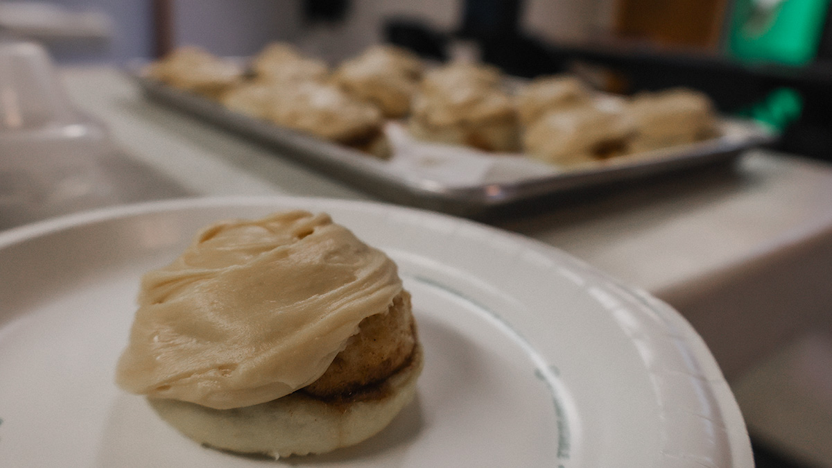 Close-up of a frosted cinnamon roll on a white plate, perfect for Cinnamon Roll Monday.