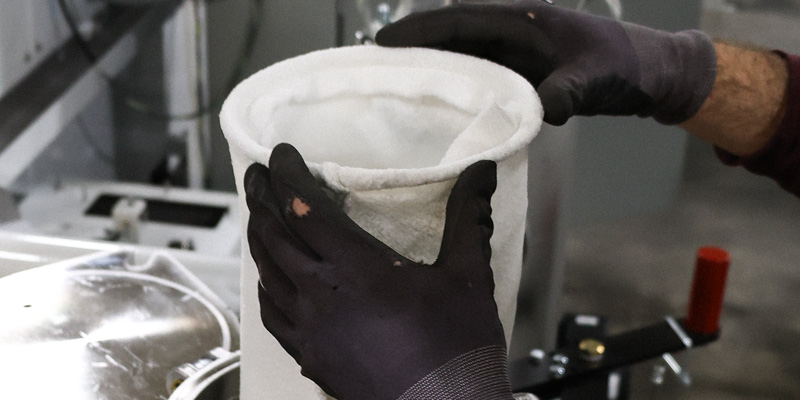 Gloved hands installing a filter bag during parts washer maintenance